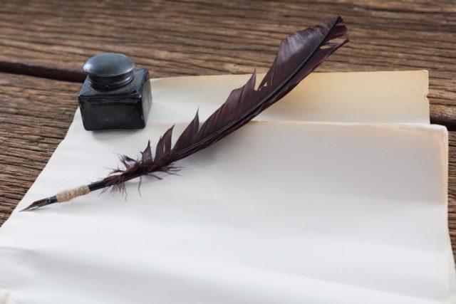 Quill feather, ink bottle and blank document on wooden table