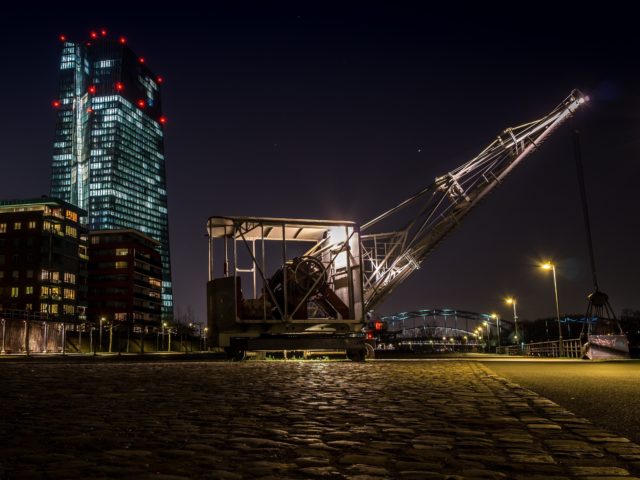 Horizontal shot of a crane in front of high building with lights at night time under the starry sky